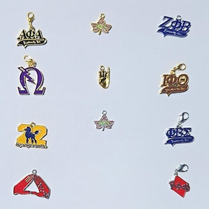 Peut inclure: Une collection de dix breloques en métal représentant divers symboles de lettres grecques, des logos de fraternités et sororités, un geste de la main et une feuille de lierre. Les breloques incluent des accents en émail doré, argenté, bleu, violet, jaune et rouge avec des fermoirs mousquetons.