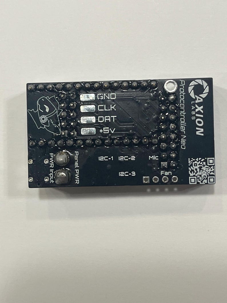 May include: A black Protocontroller Neo circuit board with white text and a logo. The board has various connection points labeled GND, CLK, DAT, and +5V. Additional labels include PWR Input, Panel PWR, I2C-1, I2C-2, I2C-3, Mic, and Fan.