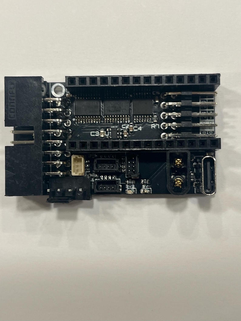 May include: A black circuit board with various electronic components, including chips, connectors, and pins. The board has the text "CONIFLY" printed on the side. It features multiple ports and a USB-C connector.