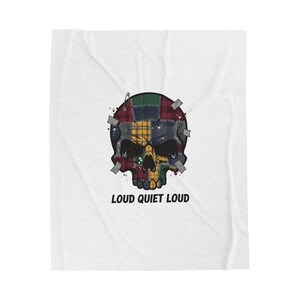 May include: A white blanket featuring a skull design. The skull is composed of patchwork in various plaid patterns, with the text "LOUD QUIET LOUD" below. The skull is decorated with tape and a safety pin.