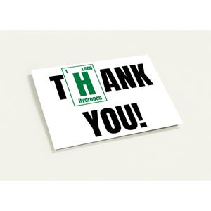 Può includere: Una carta bianca con le parole "THANK YOU!" in grassetto nero. La lettera "H" è sostituita da un riquadro verde contenente il simbolo dell'elemento Idrogeno. La carta è su una superficie bianca.