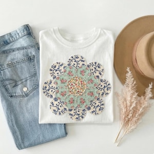 以下が含まれることがあります： 手書き風の「But First, Coffee」の文字が入った、黒い持ち手の白いセラミックマグカップ。白い表面に置かれています。 温かい飲み物用です。