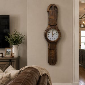 Puede incluir: Un reloj de pared alto de madera con una esfera redonda y un diseño alargado único. La esfera del reloj tiene números y manecillas negros sobre un fondo blanco. El reloj es de madera marrón oscuro y está montado en una pared beige claro.
