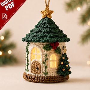 Puede incluir: Un adorno navideño de ganchillo con forma de casita con techo verde, una estrella amarilla en la punta y base marrón. Las paredes blancas tienen ventanas arqueadas, una puerta marrón, enredaderas verdes, bayas rojas y un pequeño árbol de Navidad.