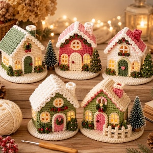 Può includere: Cinque case in miniatura realizzate all'uncinetto con colori festivi come rosso, verde e crema. Ogni casa presenta un tetto testurizzato, finestre ad arco e un piccolo camino. Le strutture sono illuminate dall'interno su basi bianche.