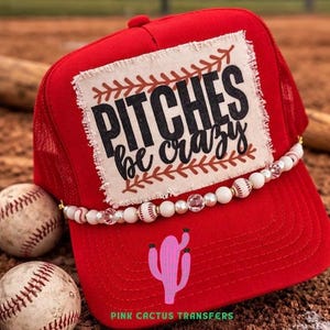 May include: Red baseball cap with a mesh back and a beaded accent. The cap features a patch with the text "Pitches be crazy" and a pink cactus graphic. Two baseballs are in the foreground.