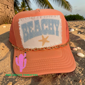 May include: A coral-colored trucker hat with a mesh back and a gold chain detail. The front patch reads "BEACHY" in blue letters with a starfish graphic. A pink cactus graphic is on the brim.