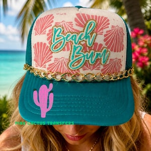 Może przedstawiać: Turkusowa czapka typu trucker ze złotym łańcuszkiem i różową grafiką kaktusa. Czapka ma napis "Beach Bum" w turkusowym i złotym brokatem, ze wzorem muszli na przednim panelu.