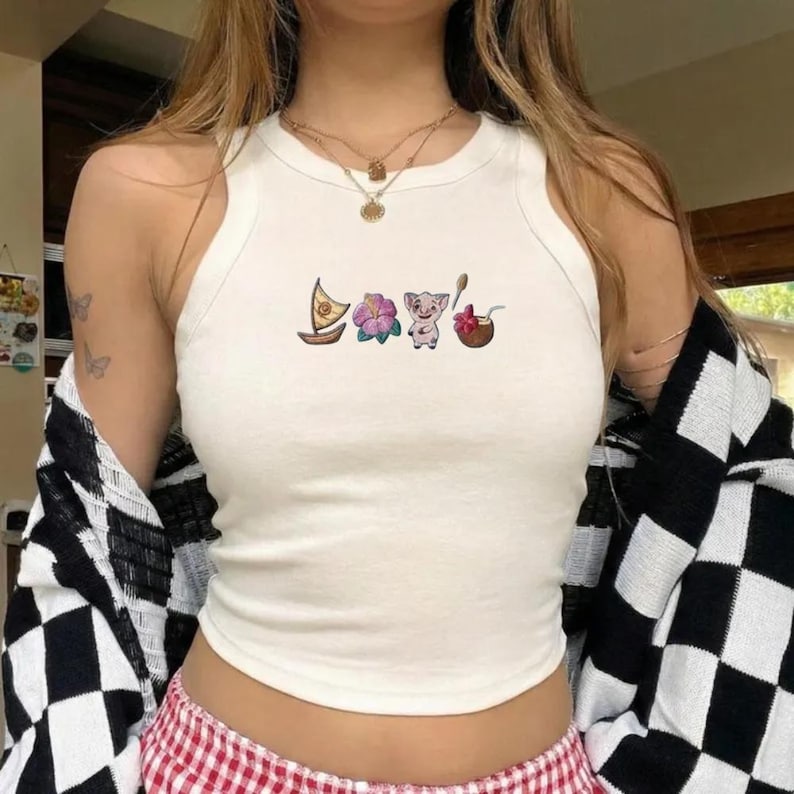 Op de afbeelding: Witte tanktop met een ronde hals en geborduurde tropische ontwerpen. Het ontwerp omvat een zeilboot, een bloem, een varken en een kokosdrankje. De top wordt gedragen met een zwart-wit geruit jasje.