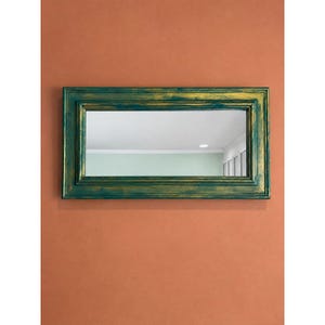 May include: A rectangular wall mirror featuring a thick, layered frame with a distressed finish that combines deep teal and metallic gold tones. The frame has a stepped, tiered profile, and the reflective glass surface shows a room interior.