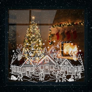 May include: A white window cling featuring a winter village scene. The design includes houses, trees, and people, with a Christmas tree and fireplace visible through the window. Snowflakes are scattered throughout the image.