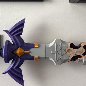 May include: A decorative sword with a purple, green, and gray handle, a silver blade, and a black tip with brown accents. The sword is mounted on a white wall, showcasing its intricate design and craftsmanship. The sword's hilt features a detailed, stylized design.