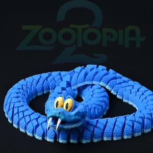 Puede incluir: Un juguete de serpiente articulada azul con una cara de dibujos animados, ojos amarillos y colmillos blancos. La serpiente está enrollada y tiene un cuerpo segmentado y texturizado. La palabra "Zootopia 2" es visible en el fondo.