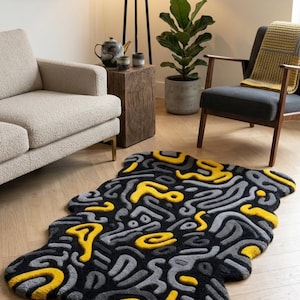 Alfombra abstracta tejida a mano, forma irregular, color negro, amarillo y gris.