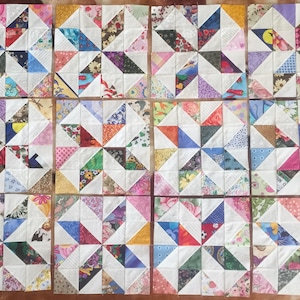 May include: A quilt made of 16 squares, each featuring a white background with a starburst pattern made of colorful fabric triangles. The quilt is made of a variety of fabrics, including floral prints, geometric patterns, and solid colors.