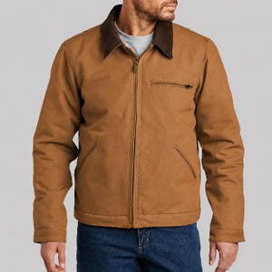 May include: A brown jacket with a dark brown collar and a zipper closure. The jacket has two front pockets and a chest pocket with a zipper. The model is wearing blue jeans.