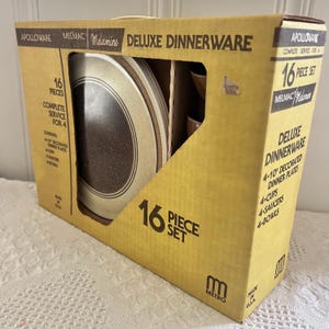 May include: A boxed 16-piece Melmac Deluxe Dinnerware set. The yellow box features black text and contains plates, cups, saucers, and bowls. The plates have a speckled brown centre with a cream-coloured border and a brown ring.