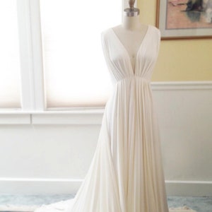 May include: A white sleeveless gown with a deep V-neckline and a flowing skirt. The gown is on a dress form and is displayed on a rug.