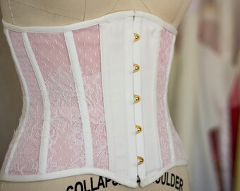 May include: White corset with pink lace detailing and gold metal clasps. The corset is made of a smooth fabric and has a boned structure.