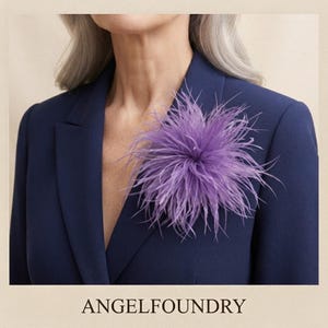 May include: A vibrant purple feather brooch pinned to a dark navy blue blazer. The accessory features a dense, circular arrangement of fine, wispy feathers that radiate outward from the center, creating a textured, voluminous floral-like appearance.