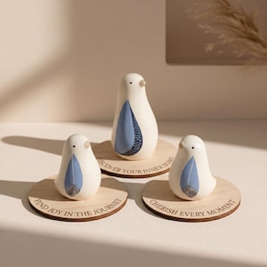 May include: Three white ceramic bird figurines with blue feather designs, each on a round wooden coaster. The coasters have engraved text: "Find Joy in the Journey", "Discover Your Inner Song", and "Cherish Every Moment".