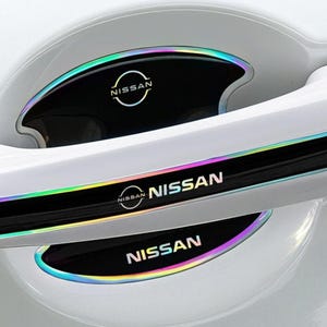 May include: A white car door handle featuring black protective decals with iridescent edges. The decals display the Nissan logo and the text NISSAN in a white font. These adhesive covers are positioned on the handle and the recessed door cup area.