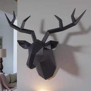 May include: A black geometric deer head wall decor. The deer head is mounted on a white wall and has a modern, angular design. The antlers are prominent, and the overall aesthetic is minimalist and contemporary.