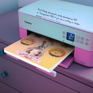 May include: A pink and white Canon Pixma printer printing a custom design. The design includes a child's photo, cartoon characters, and the text "Ophelia turns". The printer has a digital display and control buttons.