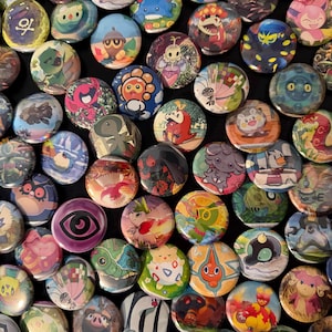 May include: A collection of colorful, round pinback buttons featuring various cartoon character designs. The buttons display a variety of colors and illustrations, with a glossy finish. The buttons are arranged closely together, filling the frame.