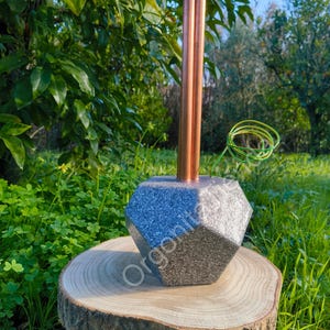 Peut inclure: Objet décoratif géométrique avec des tubes en cuivre. La base est un mélange de gris et d'argent, posée sur une tranche de bois. Le fond est un cadre extérieur naturel avec du feuillage et de l'herbe verts.