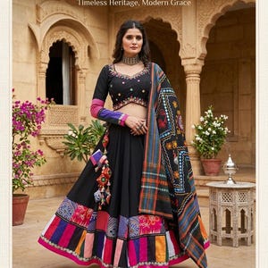 Può includere: Una donna indossa un Lehenga tradizionale Banjara nero con una camicetta e un dupatta ricamati a mano. La gonna presenta patchwork colorati e nappe. Il testo dell'immagine recita "THE KUTCH COLLECTION" e "Timeless Heritage, Modern Grace".