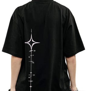 May include: A black short-sleeved t-shirt featuring a white graphic print on the back. The design consists of a vertical line intersecting a four-pointed star, with small horizontal markings and numerical text including 170, 103, 152, 130, and 127.