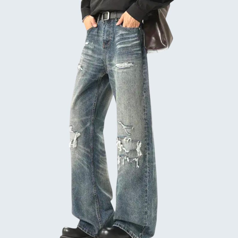May include: Faded blue denim jeans with distressed details. The wide-leg jeans feature ripped sections on the knees and thighs, a black belt, and a classic five-pocket design. The jeans have a relaxed fit and a vintage wash.