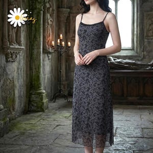 Può includere: Un abito sottoveste midi in grigio antracite scuro con motivo floreale nero, spalline sottili e un delicato bordo in pizzo lungo lo scollo. Il capo presenta una silhouette dal taglio dritto e uno strato superiore in tessuto trasparente.