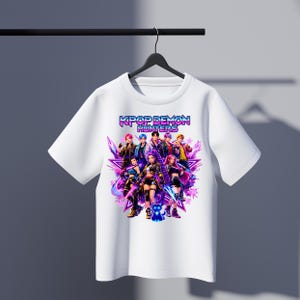 May include: White t-shirt featuring a graphic of a group of anime-style characters with the text "KPOP DEMON HUNTERS" in a vibrant, colorful design. The design includes stars and a dynamic, action-oriented composition.