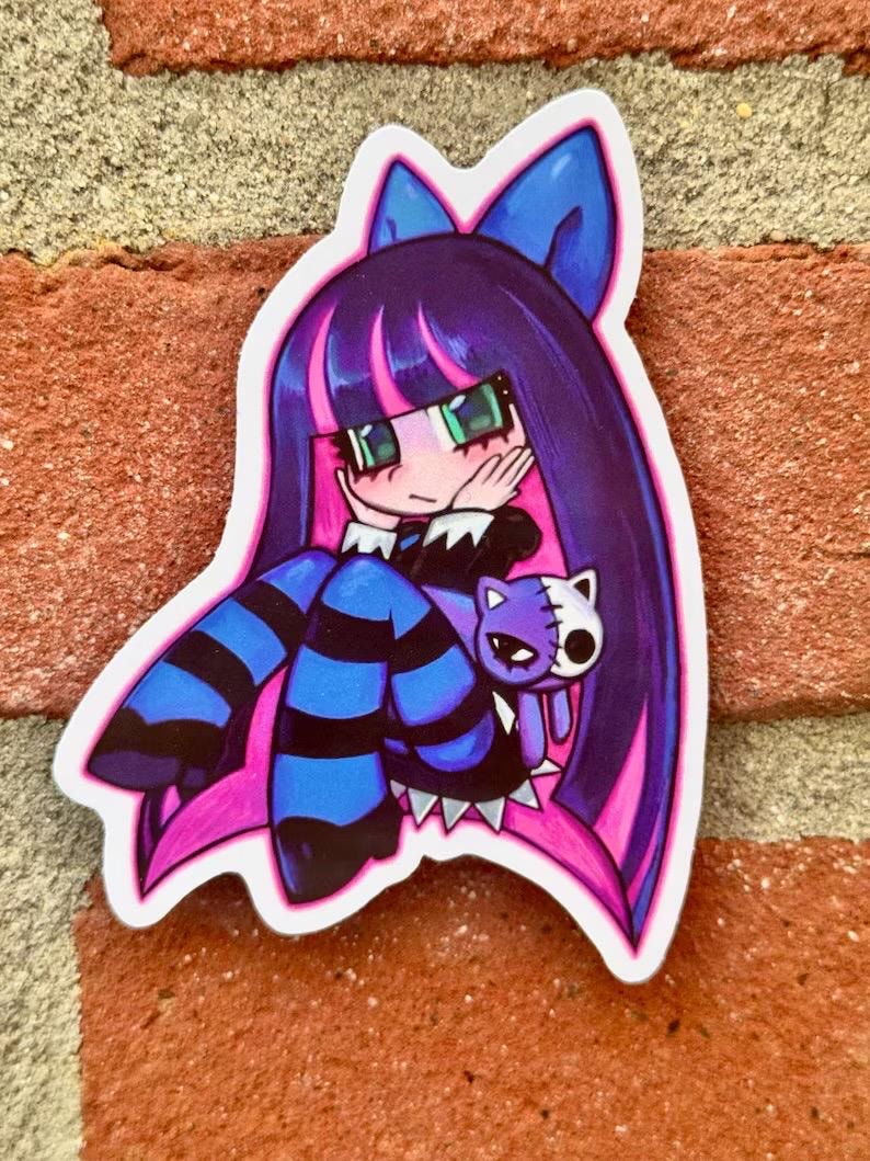 May include: A sticker depicting an anime-style character with long purple hair, a blue bow, and green eyes. The character wears a black and white outfit with blue and black striped stockings. A purple cat with a white and black face is held by the character.