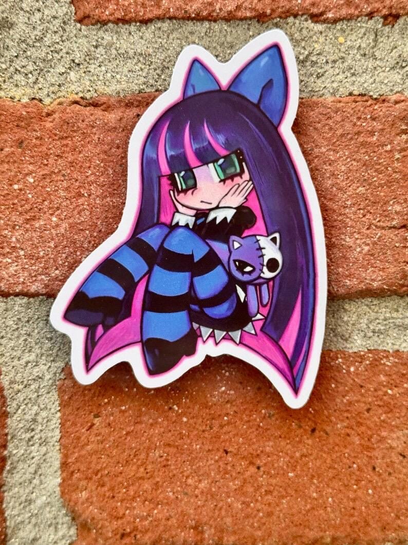 May include: A die-cut sticker depicting an anime-style character with long purple hair, pink highlights, and blue accents. The character holds a purple cat plushie. The sticker is on a brick wall.