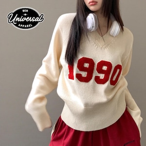 Może przedstawiać: Kremowy sweter z dekoltem w serek z numerem "1990" w kolorze czerwonym. Sweter jest połączony z czerwonymi spodniami. Obraz zawiera również logo "BEN UNIVERSAL APPAREL" w czarnym owalu.