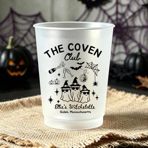 May include: A frosted plastic cup featuring black printed graphics including three ghosts wearing witch hats and sunglasses, a champagne bottle, a disco ball, a spider web, and bats. The text reads THE COVEN Club, Ellie's Witchelotte, and Salem, Massachusetts.
