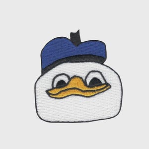 May include: Embroidered patch featuring a cartoon duck with a white body, a blue sailor hat, and a yellow beak. The patch has a black border and is likely for clothing or accessories.
