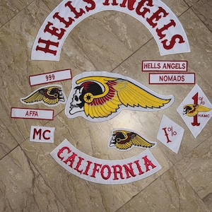 May include: A collection of white and red embroidered patches. The patches include the words "HELLS ANGELS" in a curved design, "CALIFORNIA", "NOMADS", "999", "AFFA", "MC", and "1%", along with a winged skull logo.