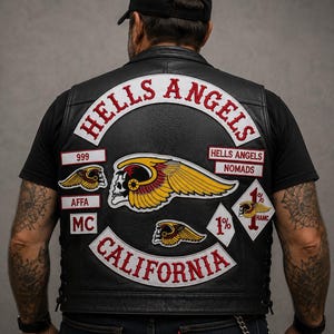 May include: Black leather vest with the words "HELLS ANGELS" in red and white lettering. Patches include "CALIFORNIA", "999", "AFFA MC", and a skull with wings. The vest is worn over a black t-shirt.
