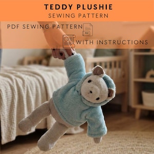May include: A plush teddy bear wearing a light blue hoodie, held up by a person. The bear has a cream-colored face and ears. Text at the top reads "TEDDY PLUSHIE SEWING PATTERN". Below, it says "PDF SEWING PATTERN WITH INSTRUCTIONS".