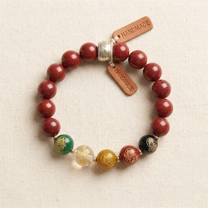 May include: A handmade bracelet with large, round, dark red beads. The bracelet incorporates accent beads in green, clear, yellow, and black, each with a decorative design. Two small tags with the word "HANDMADE" are attached.