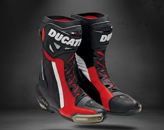 May include: Pair of black and red Ducati motorcycle boots. The boots feature the Ducati logo, white accents, and a gold-coloured plate on the toe. Designed for protection and performance.