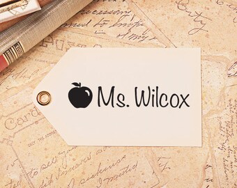 May include: A white rectangular label with a black apple and the text "Ms. Wilcox" printed on it.