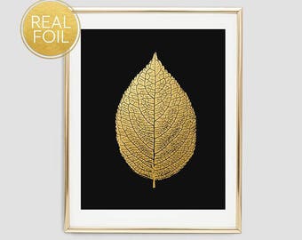May include: A framed art print featuring a gold foil leaf on a black background. The leaf's intricate veins are visible, and the frame is gold. The words "REAL FOIL" are printed on a gold circle in the upper left corner.