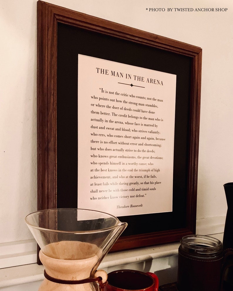 May include: A framed print with a black background and white text. The text is a quote by Theodore Roosevelt about "The Man in the Arena".