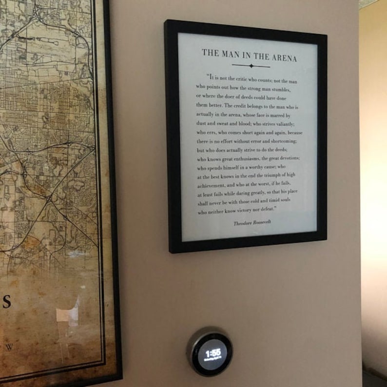 May include: A black framed print with a white background and black text. The text is a quote by Theodore Roosevelt about the "Man in the Arena". The quote is about the importance of action and striving for greatness, even in the face of failure.