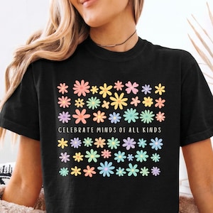 May include: Black t-shirt featuring a floral pattern in pastel colours, with the words "CELEBRATE MINDS OF ALL KINDS". The flowers are pink, yellow, blue, green, and purple. The shirt has a crew neck and short sleeves.